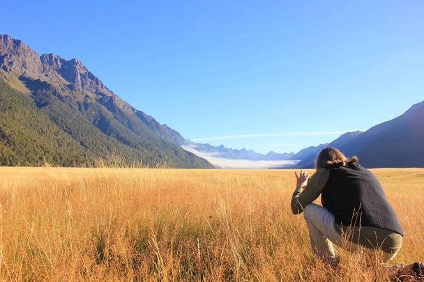 Frau kauert vor dramatischer Neuseeland-Landschaft und fotografiert mit ihrem Handy - Foto, Bild