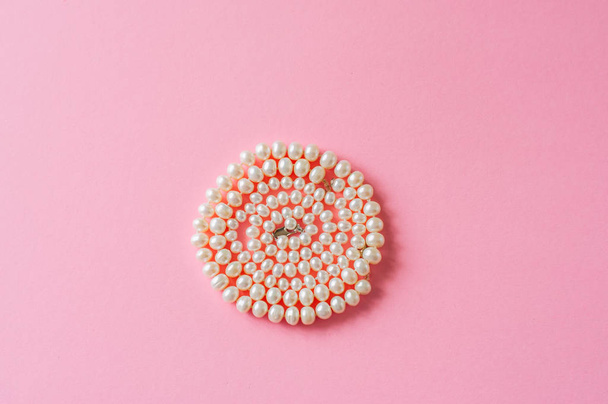 Wedding or fashion concept. Pearl necklace on a pink background. Toned. - Foto, imagen