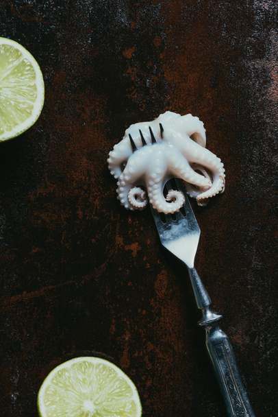 top view of little octopus on fork on rusty metal surface with limes - Photo, Image