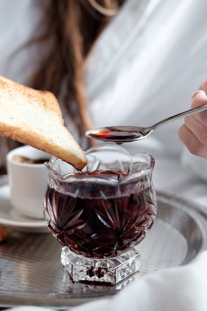 Breakfast in bed in hotel. Spoon spreading cherry jam on a toast. - Photo, Image
