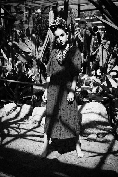 Чорно-біла фотографія чудової молодої жінки в елегантній сукні і квітковій головній убірці позує
 - Фото, зображення