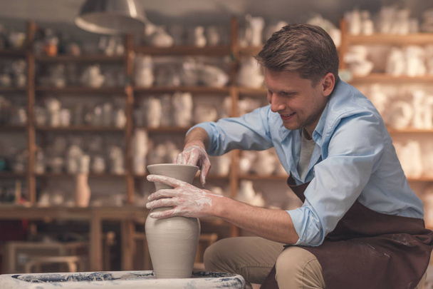 A young man behind a potter's wheel in pottery - Photo, Image