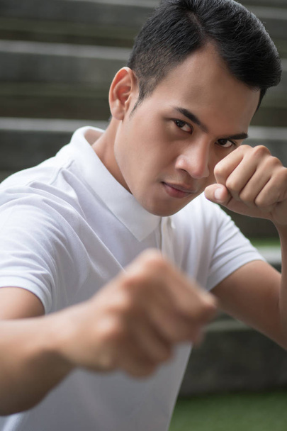 сильный мужчина сжимая свой кулачный портрет; человек боец в кулачном бою позируют глядя на вас; азиатский молодой мужчина модель
 - Фото, изображение
