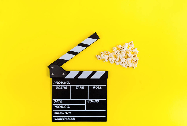 Cinema background. Film watching. Popcorn and clapperboard on yellow background top view copy space - Фото, изображение