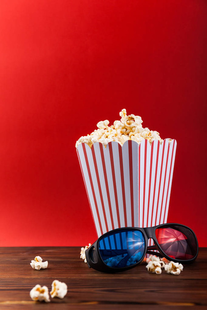 Cinema background. Film watching. Glasses, drink, popcorn and clapperboard on red background top view copy space - Photo, Image