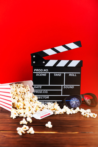Cinema clapperboard, popcorn, tickets and 3d glasses on wooden planks with copy space - Photo, Image
