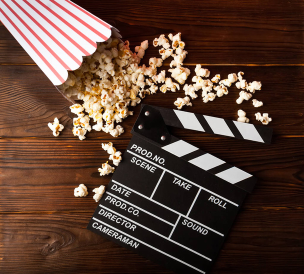 Cinema background. Film watching. Popcorn and clapperboard on wooden planks with copy space - Photo, Image