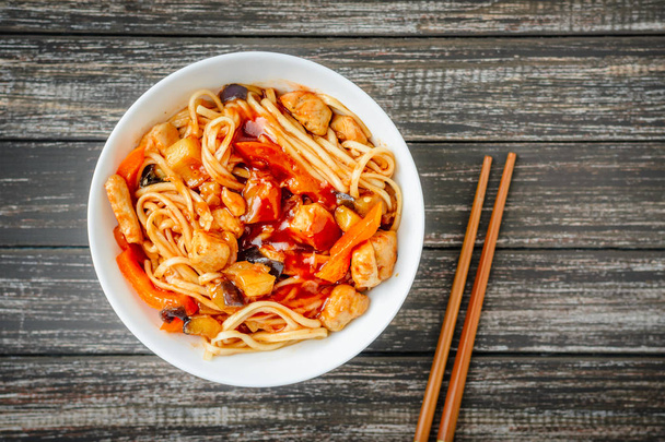 noodles udon in sweet and sour sauce and chopsticks on wooden table, top view. Traditional Asian cuisine - Photo, Image
