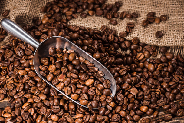 close-up shot of scoop and roasted coffee beans spilled on sackcloth - Фото, изображение