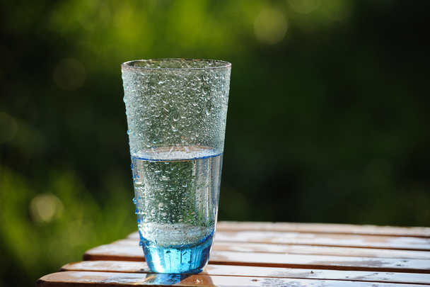Bicchiere di acqua minerale fredda sul tavolo sullo sfondo della natura
 - Foto, immagini
