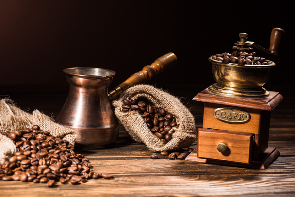 vintage cezve and coffee grinder on rustic wooden table spilled with roasted beans - Foto, afbeelding