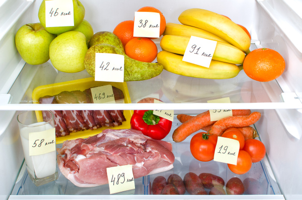 Open fridge full of fruits, vegetables and meat with marked calories - Photo, Image