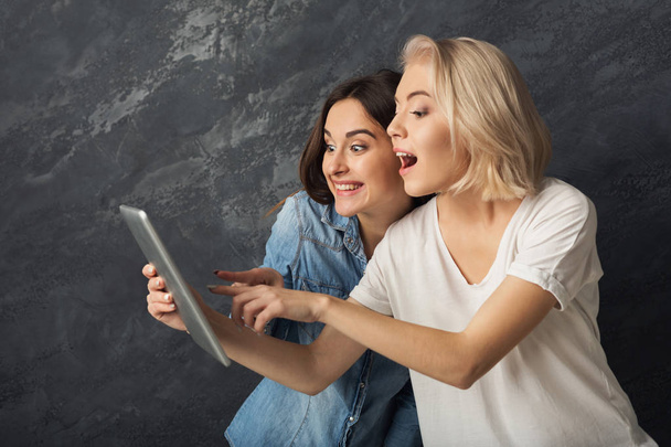 Curious female friends using tablet at dark studio background - Photo, image
