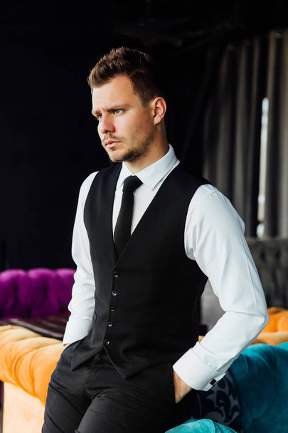 Stylish athletic man in a business costume vest. Sits in the turquoise sofa chair, a serious look. - Foto, Imagem