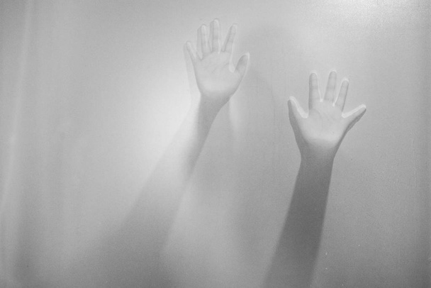Schaduw van de handen van de vrouw achter matglas. Wazig hand abstractie. Halloween achtergrond. Zwart-wit foto - Foto, afbeelding