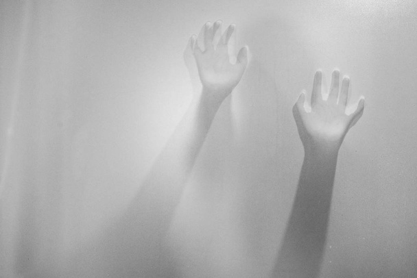 Shadow hands of the woman behind frosted glass.Blurry hand abstraction.Halloween background.Black and white picture - Photo, Image
