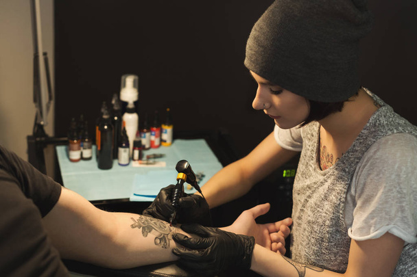 Mujer joven tatuadora haciendo tatuaje en brazo masculino
 - Foto, Imagen
