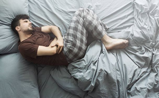 Mies makaa sängyssä ottaa vatsakipu, ylhäältä katsottuna
 - Valokuva, kuva