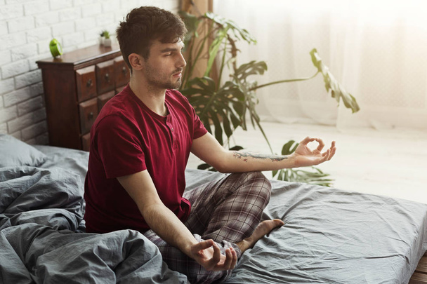 蓮のポーズでベッドに座っている若い男 - 写真・画像