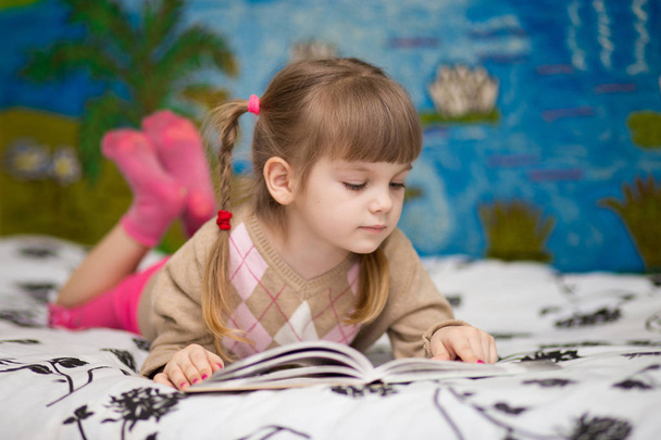 Petite fille joyeuse lire le livre au lit. Concept de connaissance des enfants
 - Photo, image