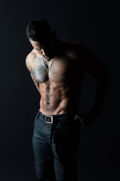 Bodycare with fitness and sport. Man with tattoo design on skin. Bearded man shirtless with fit torso. Fashion model put leather belt on jeans. Sportsman with tattooed arm and chest - Foto, Bild