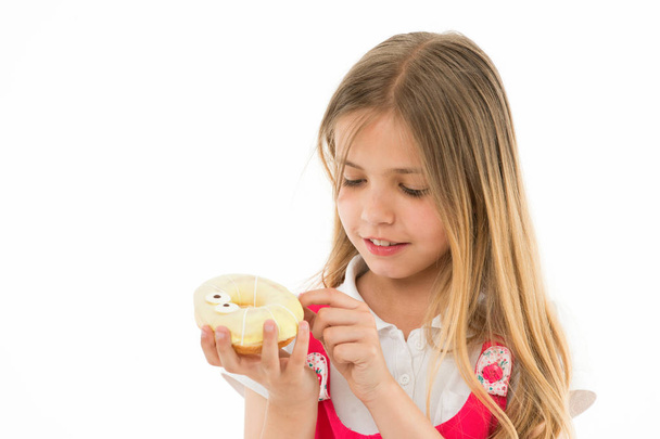 Sweet treasure. Girl calm face carefully holds sweet donut in hand, isolated white. Kid girl with long hair likes donuts. Snack concept. Child likes to eat donuts with colorful toppings, copy space - Photo, Image