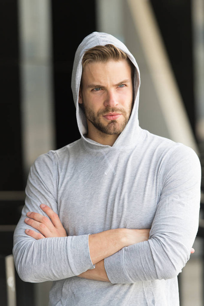 Cool and confident. Man unshaven hooded folded arms looks handsome and cool. Guy bearded attractive cares about appearance. Man bristle serious face, urban background, defocused. Metrosexual concept - Fotoğraf, Görsel