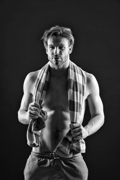 Sexy athlete with towel on neck after training. Sportsman with muscular chest and belly. Fitness man with fit torso in shorts. Sport and wellness. Hygiene or health and bodycare, black and white - Photo, image