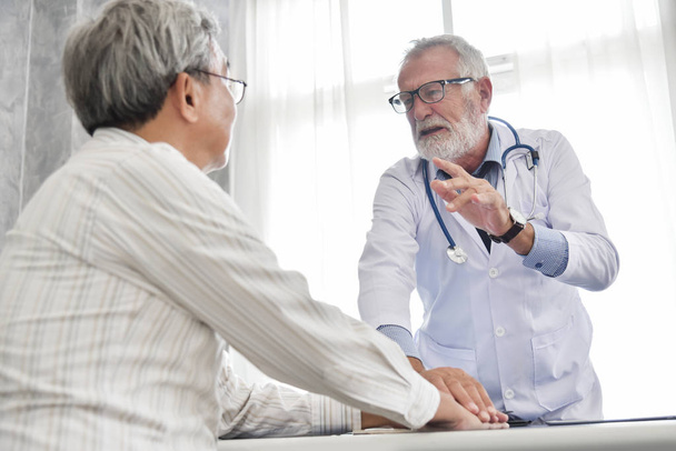Senior maschio medico sta discutendo con asiatico maschio paziente in il medico stanza
. - Foto, immagini
