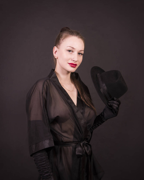 Beautiful young girl with long hair, black tunic, black gloves and black hat.Posing in the Studio on a dark background, isolated images. - Foto, immagini