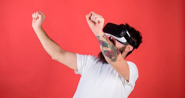 Man with beard in VR glasses driving motorbike, red background. Virtual driving lessons concept. Hipster on excited face driving bike on high speed in virtual reality with modern digital gadget - Foto, Imagem