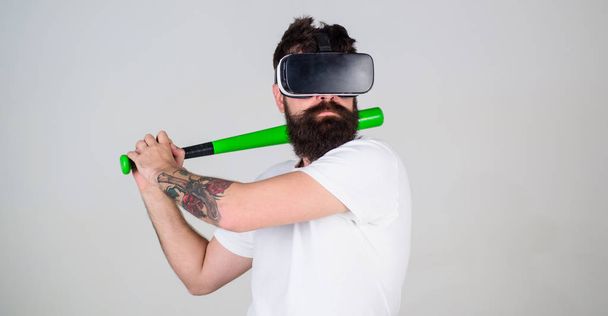 Man in VR glasses with hipster beard and tattoo posing with baseball bat isolated on gray background. Amateur player training batting skills in simulation game. Bearded man doing sports - Foto, afbeelding