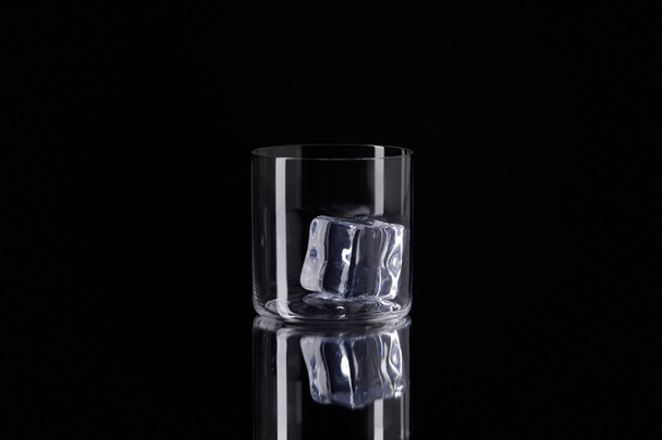 glass with ice cube on reflective surface isolated on black - Photo, Image
