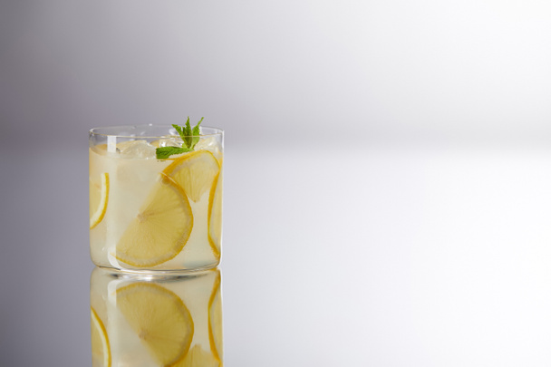 ein Glas frische Limonade auf reflektierender Oberfläche und auf grau - Foto, Bild