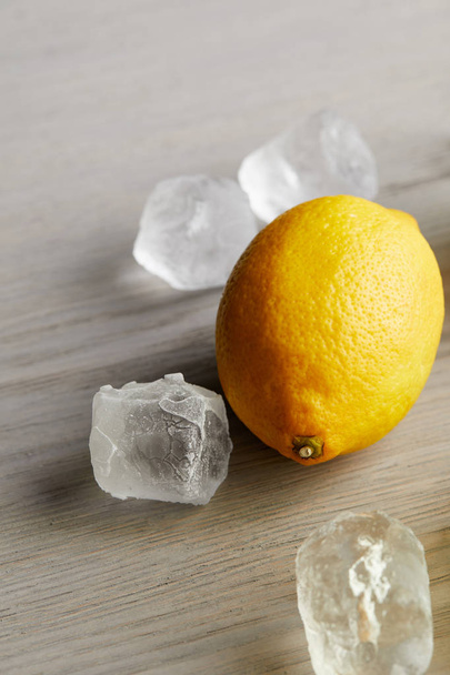 Detailní záběr zralého citrónu a kostky ledu na dřevěný povrch - Fotografie, Obrázek
