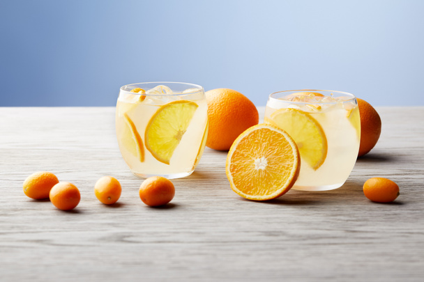 glasses of delicious lemonade with ripe oranges on wooden tabletop - Фото, изображение