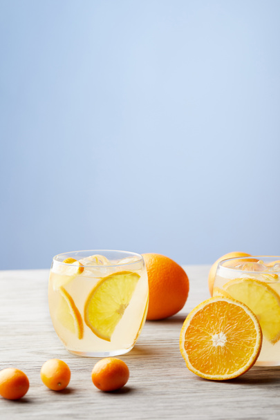 glasses of cooled delicious lemonade with ripe oranges on wooden tabletop - Fotoğraf, Görsel