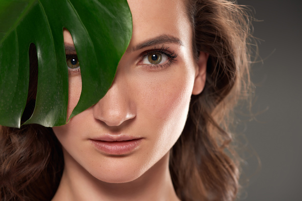attractive pure girl with monstera leaf, isolated on grey  - Foto, Imagem