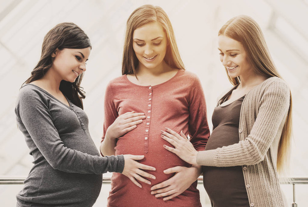 Two cheerful women touching their pregnant friend - 写真・画像