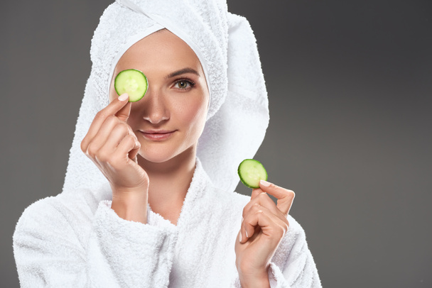 attractive girl with cucumber slices in white bathrobe and towel, isolated on grey - Fotografie, Obrázek