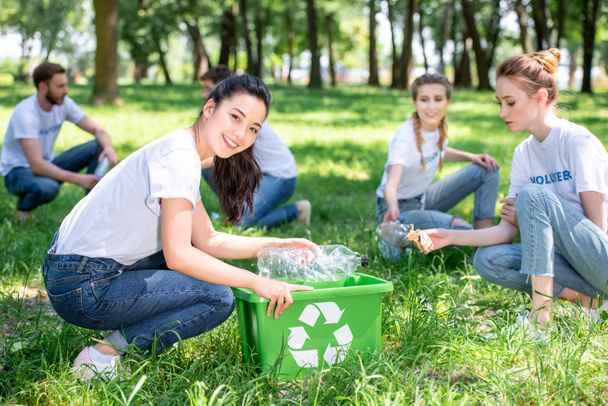 Jovens voluntários sorridentes limpando o parque com caixa de reciclagem
  - Foto, Imagem