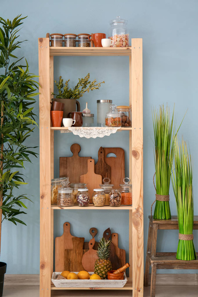 Wooden storage stand with kitchenware and different foodstuff indoors - Foto, afbeelding