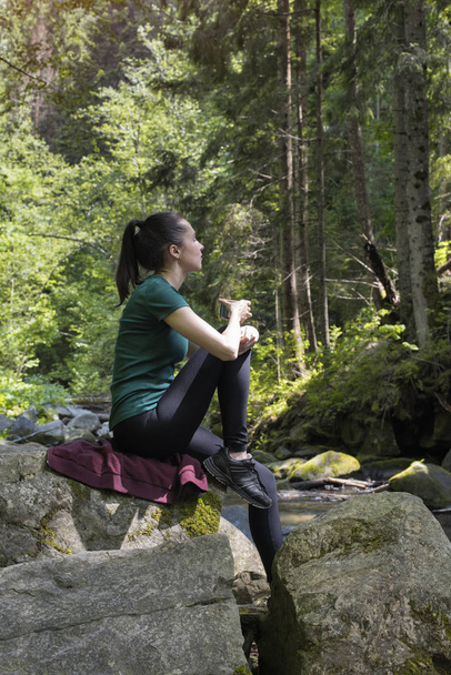 Κορίτσι με ένα φλιτζάνι τσάι κάθεται σε έναν βράχο στο δάσος. Μέρα του καλοκαιριού - Φωτογραφία, εικόνα