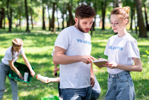 Ehepaar schaut Lehrbuch an, während Freiwillige Park säubern   - Foto, Bild