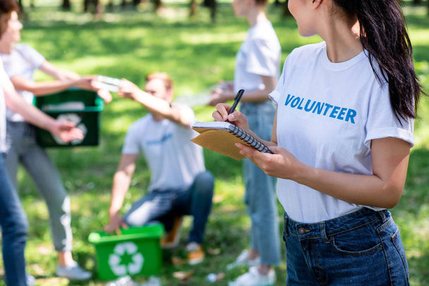 woman writing in textbook while volunteers cleaning park   - Photo, Image