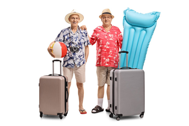 Full length portrait of two elderly tourists with a beach ball, an air mattress and suitcases isolated on white background - Photo, image