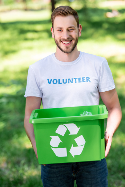 smiling male volunteer holding recycling box with rubbish in park - Fotó, kép