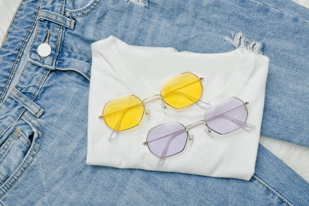 Multicolored sunglasses on a white T-shirt and jeans. Fashionable concept - Photo, Image