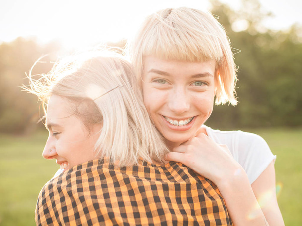 Two cheerful young women are hugging on the field. Close up. - 写真・画像