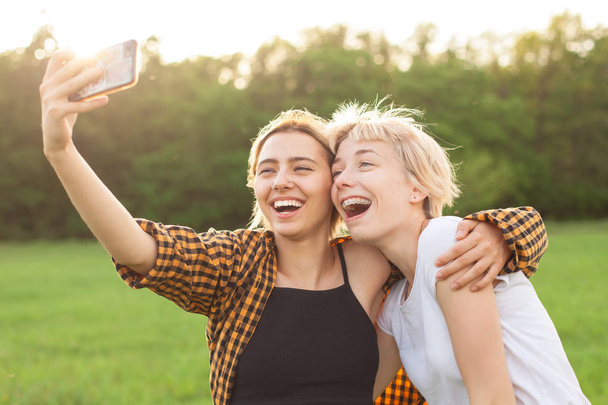 Twee vrolijke jonge vrouwen maken selfie op mobiele telefoon - Foto, afbeelding